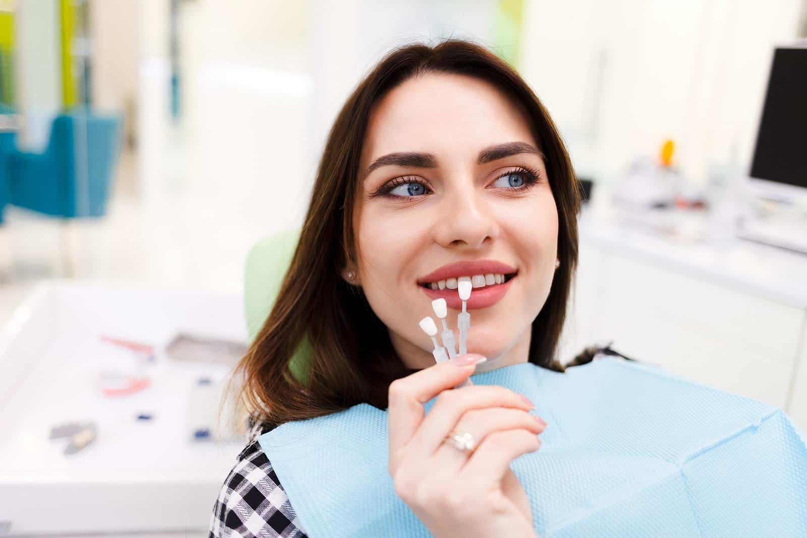 Woman matching her teeth to a veneer shade guide in a dental office