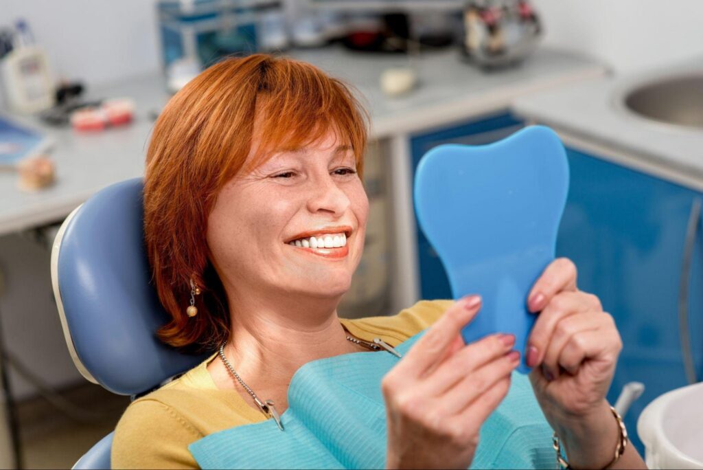 Senior woman smiling at her teeth in a mirror after a dental procedure